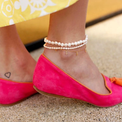 A woman's foot displaying a large pearl anklet, a small pearl anklet, and a dainty gold anklet.