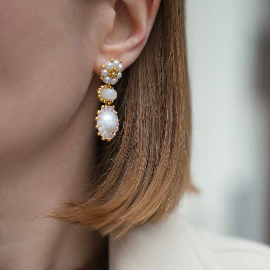 Detailed view of an ear with rose gold earring, pearls and gemstones