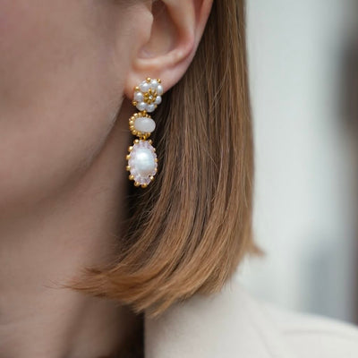 Detailed view of an ear with rose gold earring, pearls and gemstones