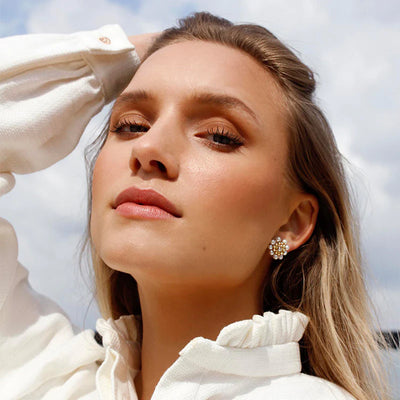 A woman standing in front of a sunny sky showing off real pearl earrings.