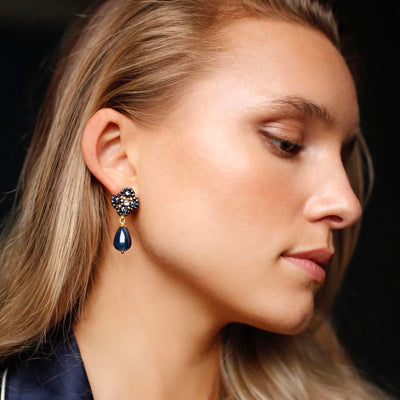 A woman wearing dark blue drop earrings with natural stones, beads, and real pearls.