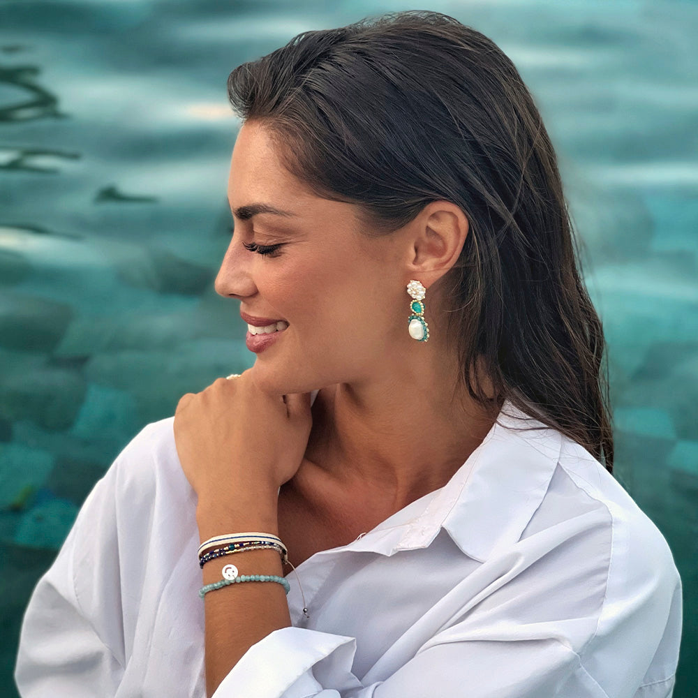woman wearing turquoise gemstone statement earrings and gemstone bracelet with mother of pearl smiley charm in the water