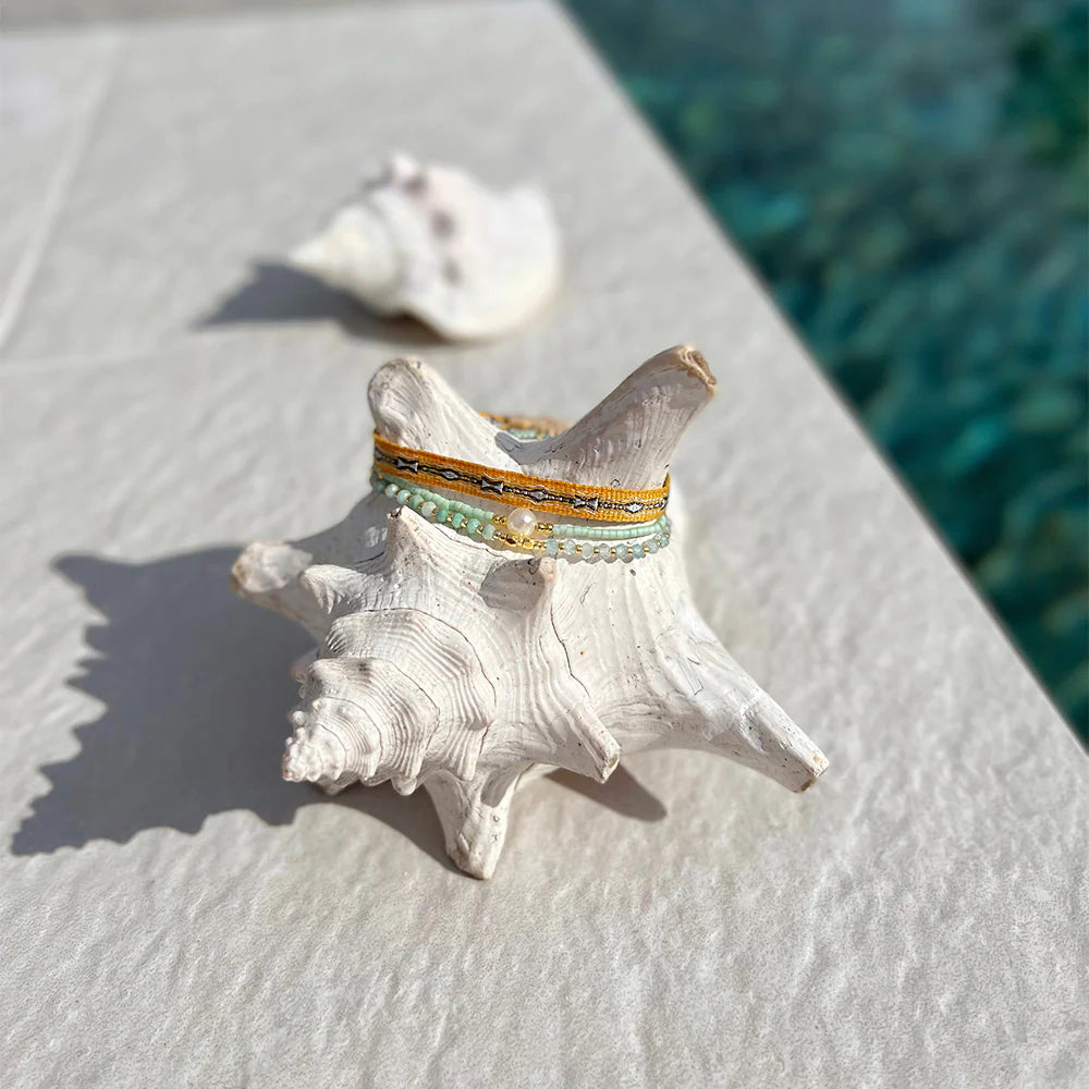 Pool-side vibes: a 3-strand green bracelet displayed on a shell.
