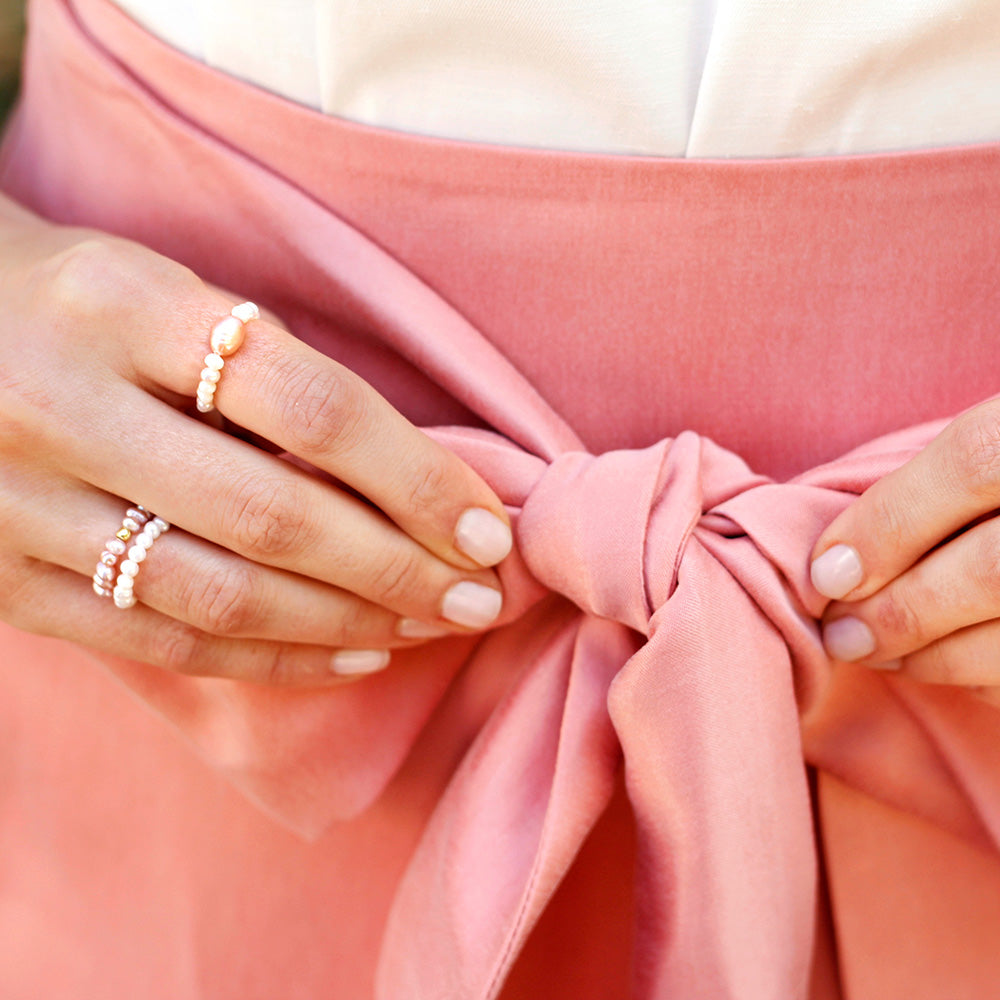 Stretchringe aus kleinen fliederfarbenen und rosafarbenen Süßwasserperlen und einer 18 Karat vergoldeten Perle kombiniert mit einem fair-fashion Rock von Consches.