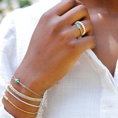 Stretchring aus kleinen weißen Süßwasserperlen und einer 18 Karat vergoldeten Perle kombiniert mit weißem Consches Kleid.