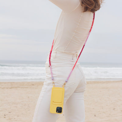 Wear a white beach outfit with a sunny yellow phone case and a berry and lilac phone chain necklace.