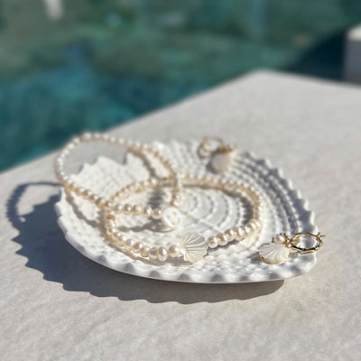 Schimmernde weiße Schmiuckstückstücke, aus zeitlosen Perlen formen moderne Schmuckstücke, die auf einem coolen Teller im Seeigel Look präsentiert sind.