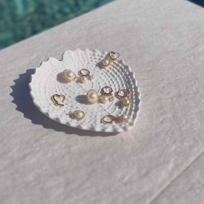 Diverse Perlenhoops, präsentiert auf einem weißen Porzellanteller, dem Sommertrend 2023 entsprechend.